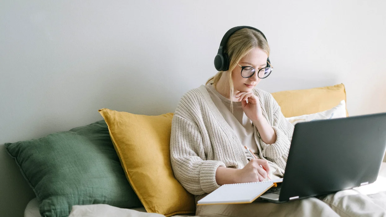 a woman wearing headphones and sitting on a couch with a laptop